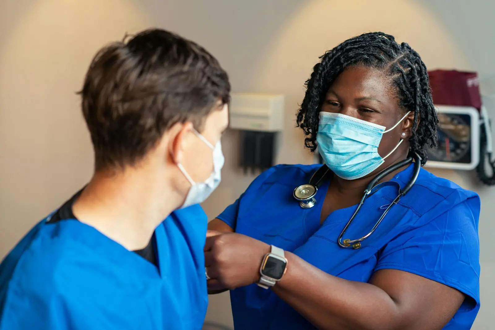 Two healthcare workers in scrubs supporting a patient